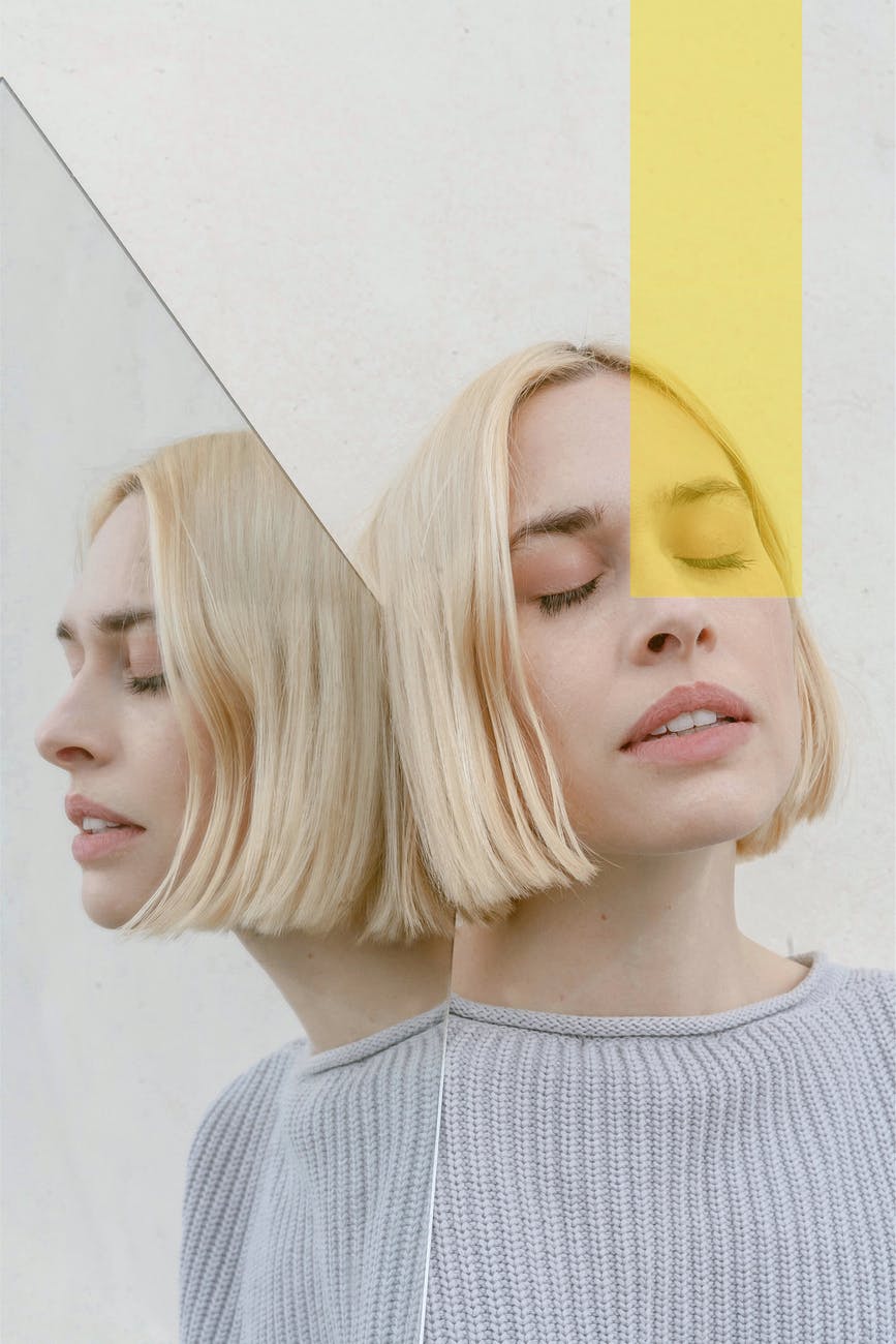 pensive young woman with closed eyes reflecting in mirror