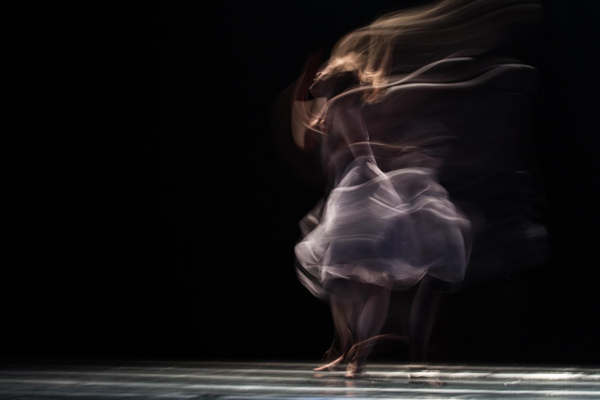 Intuitive Movement: Featured image for "What is Intuitive Movement? (Tips & Techniques for Stretching & Ecstatic Intuitive Movement) : depicts a woman dancing in such a fast and fluid way that she cannot be captured by the image, instead disappearing outward into swirls and fluid movement.
