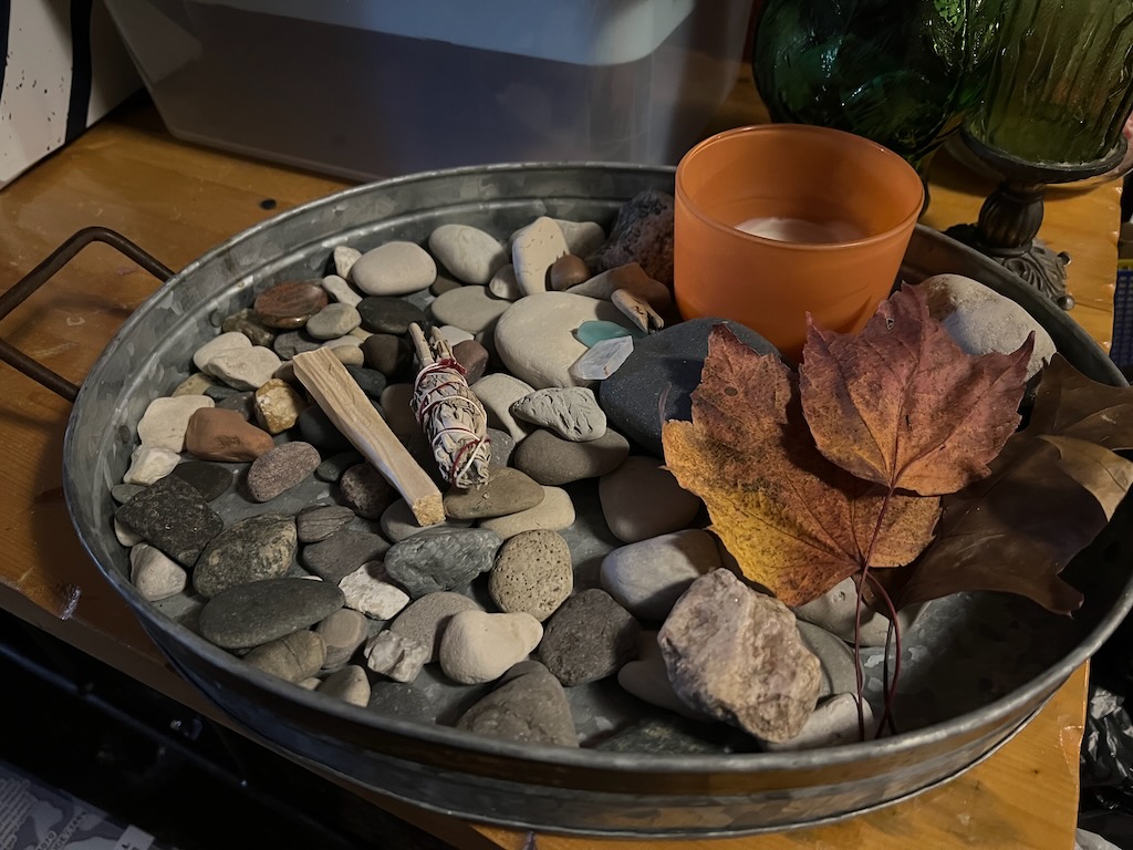 a tray of rocks collected and displayed with leaves and a candle. The stones symbolize the polished stones in the parable of the jagged stones or discussing what time heals all wounds means